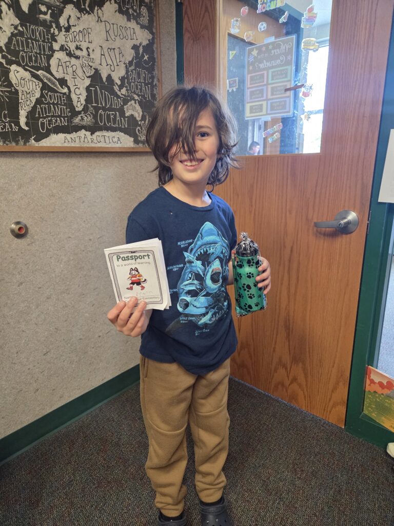 A child with long hair smiles while holding a passport and a water bottle, standing by a door with a world map.