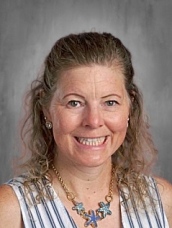 Smiling woman with curly hair, wearing a striped top and necklace, against a gray background.