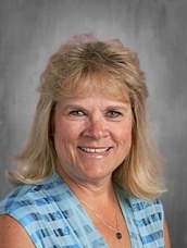 Smiling woman with blonde hair, wearing a blue patterned top, against a gray background.