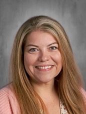Woman with long blonde hair and a pink top smiling against a gray background.