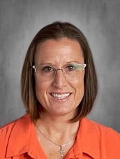 Woman with glasses and shoulder-length brown hair, smiling, wearing an orange shirt and a cross necklace.
