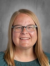 A person with long hair and glasses smiles against a neutral background.