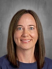 A person with shoulder-length brown hair smiling against a gray background.