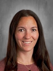 Woman with long dark hair smiling against a gray background.