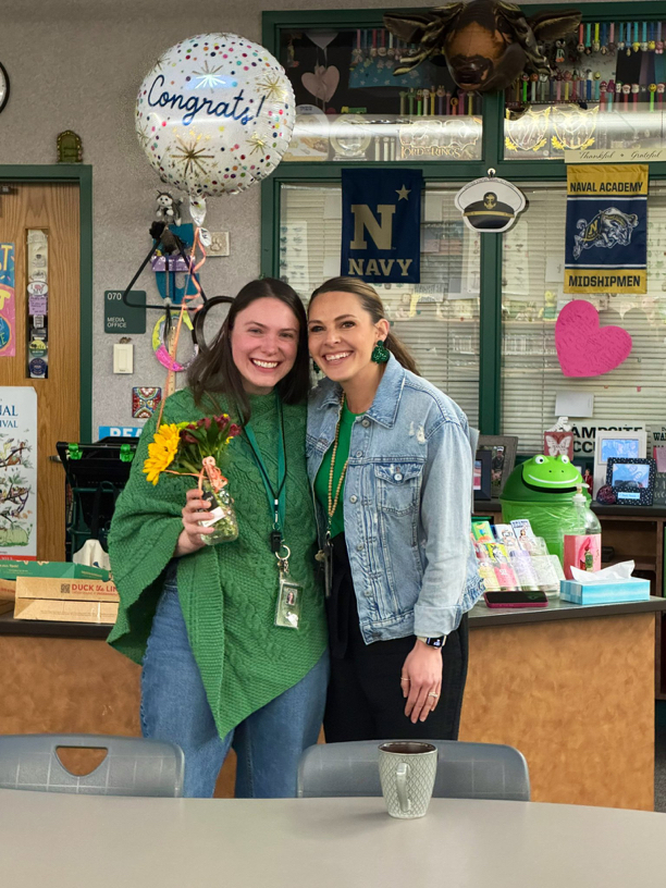 Two women stand together, smiling. One holds a bouquet of flowers; a "Congrats!" balloon floats above them.