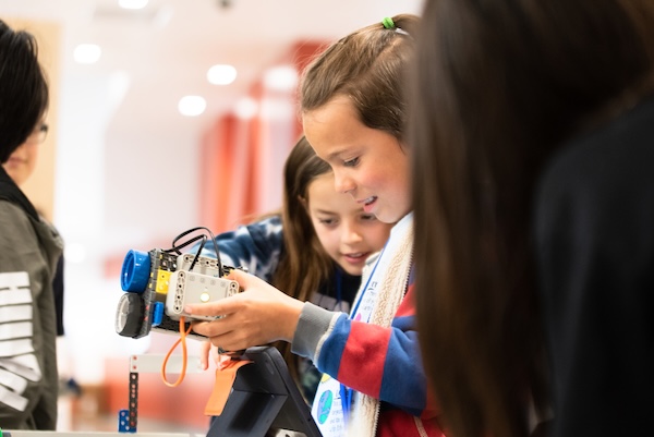 Two children examine a robotic device, engaged in a learning activity in a classroom setting.