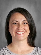 Smiling woman with long dark hair, wearing a light gray top, against a neutral background.