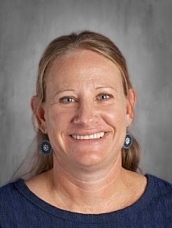 Smiling woman with long blonde hair, wearing a blue shirt and earrings, against a neutral background.