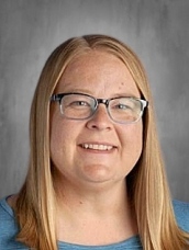 Smiling woman with long straight hair and glasses, wearing a blue shirt, against a gray background.