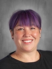 Smiling woman with short purple hair, wearing a black shirt, against a gray background.