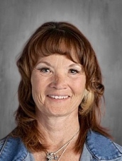 Smiling woman with medium-length brown hair, wearing a denim jacket, set against a gray background.