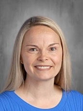 Smiling woman with long blonde hair, wearing a blue sweater, against a gray background.