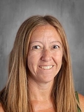 A smiling woman with long brown hair, wearing a green top, against a gray background.