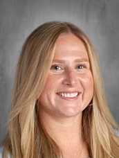 Mujer sonriente de pelo largo y rubio, con camisa clara, sobre fondo gris.