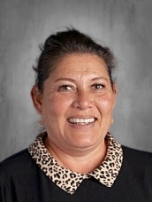 Smiling woman with dark hair, wearing a black shirt with a leopard print collar, against a gray background.