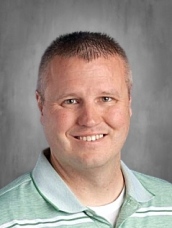 Hombre sonriente de pelo corto castaño claro vestido con un polo a rayas verdes y blancas sobre fondo gris.