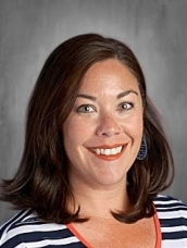 A woman with shoulder-length brown hair, wearing a striped shirt, smiles in front of a neutral background.