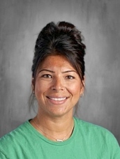 A woman with dark hair styled in a bun, wearing a green shirt, smiles against a gray background.