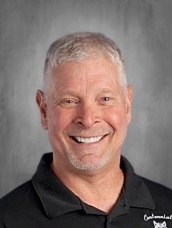 Smiling middle-aged man with short gray hair, wearing a black shirt, against a gray background.
