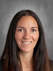 Headshot of a woman with long dark hair, smiling, against a neutral gray background.