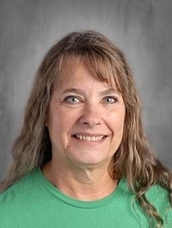 Smiling woman with long, wavy hair wearing a green shirt, set against a neutral background.