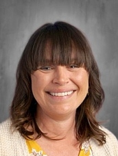 Smiling woman with brown hair and bangs, wearing a yellow top and a light cardigan, set against a neutral background.