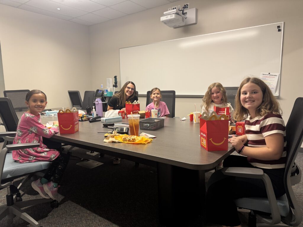 Five children are sitting around a table in a meeting room, enjoying McDonald's Happy Meals and drinks.