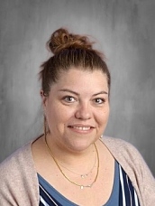 Smiling woman with brown hair in a bun, wearing a striped top and a light cardigan, against a gray background.