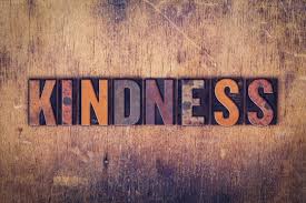 The word "KINDNESS" spelled out in bold, textured letters on a rustic wooden background.