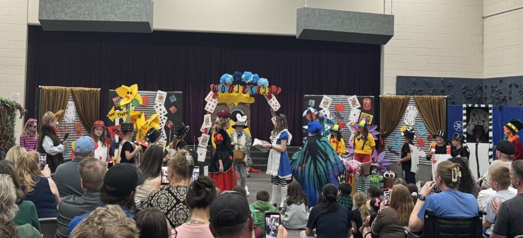 A colorful stage performance with children in costumes, featuring a whimsical backdrop and an audience watching.